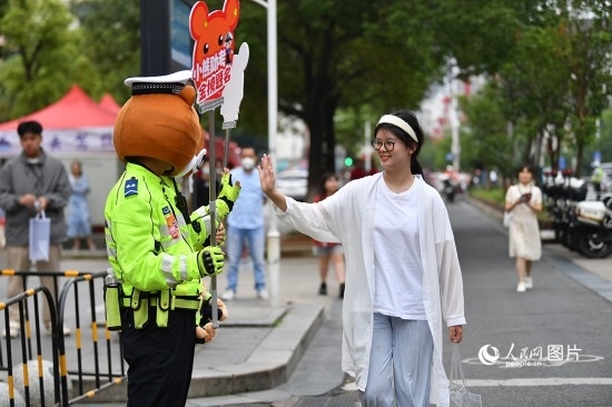6月7日上午9時，隨著鈴聲的響起，2023年江西高考正式開考，江西省的53.57萬考生以縣（區(qū)）為單位隨機安排在全省256個考點、18968個考場參加高考。圖為“小熊交警”和考生擊掌鼓勵。 人民網(wǎng)記者 時雨攝