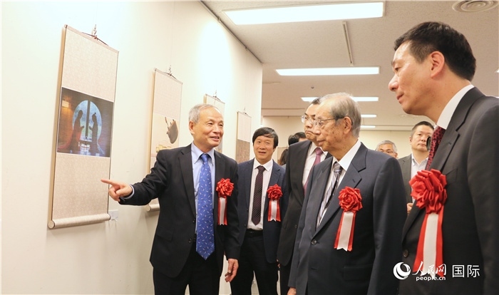 “湖州印象”攝影展主創(chuàng)、世界華人攝影協(xié)會副會長馮學(xué)敏向吳江浩大使、福田康夫前首相等嘉賓介紹展出作品。（人民網(wǎng) 許可攝）