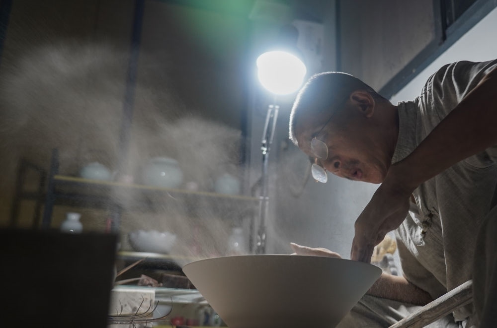 ↑ 在景德鎮(zhèn)，手工匠人吹去坯內(nèi)的泥土（2021年7月14日攝）。