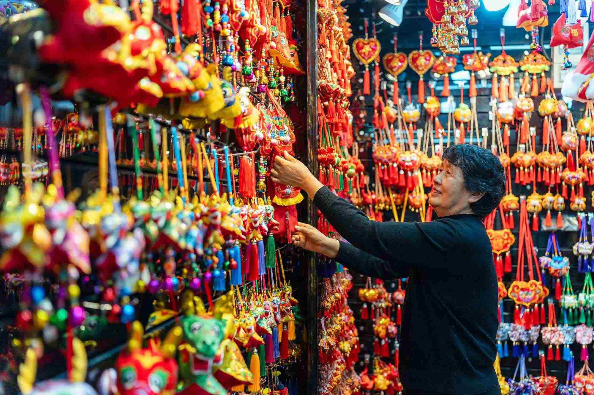 2023年12月11日，金華義烏國際商貿(mào)城，龍年喜慶用品掛滿攤位，顧客正在挑選中。