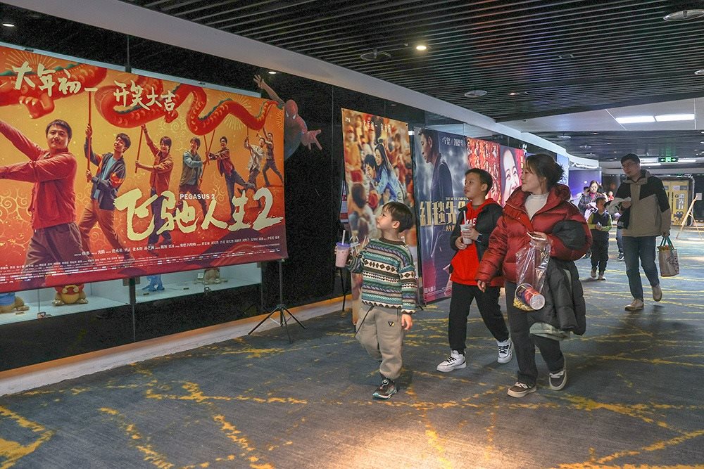 △ 2024年2月16日，在江西贛州一家電影院，觀眾從春節(jié)檔電影的宣傳展板前走過。