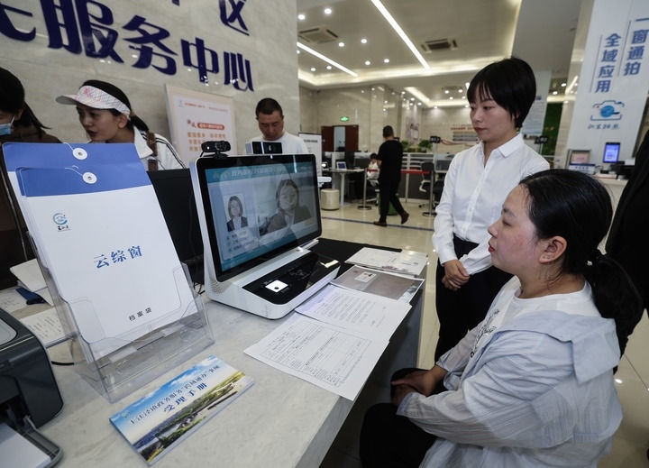 在浙江省嘉興市秀洲區(qū)王江涇鎮(zhèn)便民服務(wù)中心的“跨域通辦·云綜窗”窗口，辦理開業(yè)登記的個體工商戶（右一）通過該系統(tǒng)與江蘇省蘇州市吳江區(qū)盛澤鎮(zhèn)行政審批局工作人員視頻連線，進(jìn)行身份讀取及材料線上審核（2024年5月9日攝）。新華社記者 徐昱 攝