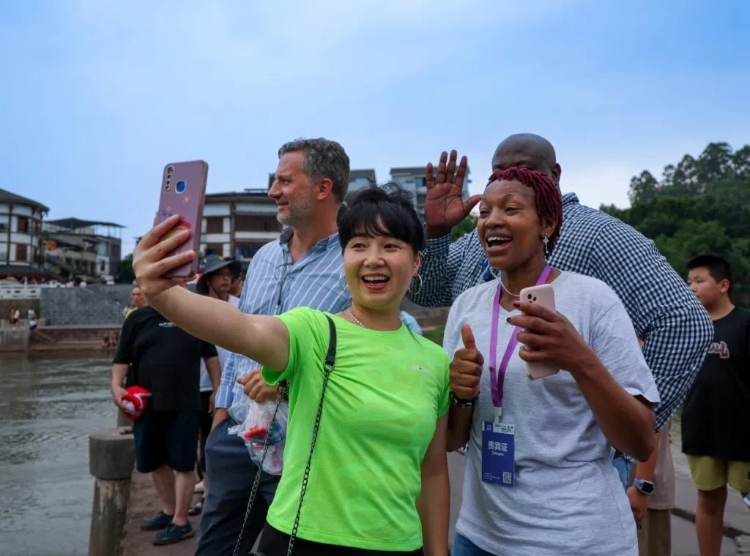 2024“一帶一路”媒體合作論壇聯(lián)合采訪調(diào)研行成員在樂山蘇稽古鎮(zhèn)與游客合影留念。本報記者 伊霄攝