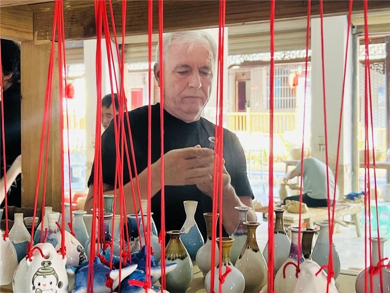 鄉(xiāng)愁如同一根根紅線，將游子與故鄉(xiāng)永遠(yuǎn)地牽連到一起。花茂村陶藝文化創(chuàng)意一條街的母氏陶藝館內(nèi)，紅線吊著陶瓶，思緒游走萬(wàn)里。摩爾多瓦“信息標(biāo)簽”通訊社社長(zhǎng)亞歷山大·塔納斯端詳著館內(nèi)展示的陶藝作品，并挑選出心儀的小擺件帶回摩爾多瓦，也帶走花茂村的“鄉(xiāng)愁”。（張亞欣攝）