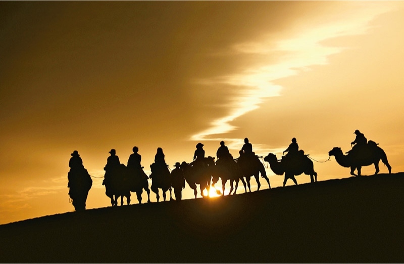 新時代以來，文化和旅游深度融合發(fā)展體制機(jī)制不斷健全，成功走出了一條獨(dú)具特色的中國旅游發(fā)展之路。圖為2024年9月1日清晨，游客在甘肅省敦煌市鳴沙山月牙泉景區(qū)乘騎駱駝，欣賞大漠風(fēng)光，體驗(yàn)絲路風(fēng)情。 新華社發(fā) 張曉亮/攝