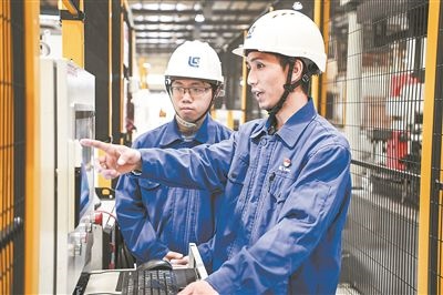 在廣西柳工機械股份有限公司生產(chǎn)車間內(nèi)，一名高級技師（右）給徒弟講解數(shù)控設備操作細節(jié)。新華社記者 曹祎銘攝