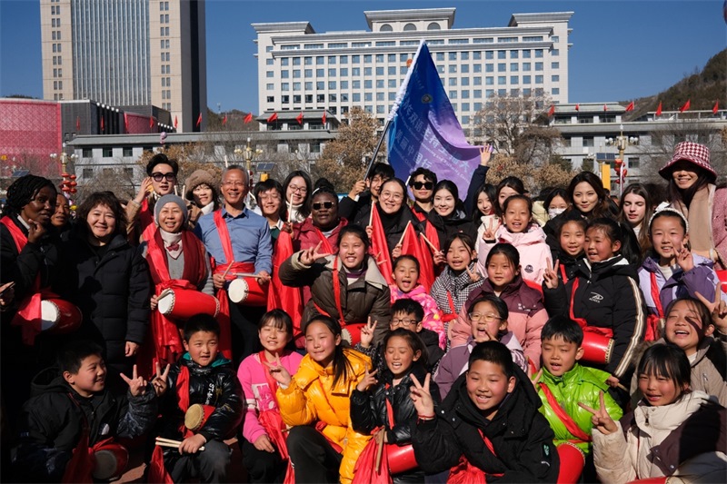 中外青年學(xué)子在安塞文化廣場觀看陜北腰鼓和大秧歌表演后合影留念，大家踏著鼓點(diǎn)共舞，翻飛的紅綢與躍動的身影交織，在黃土地廣場上繪出一幅生動的陜北民俗互動畫卷